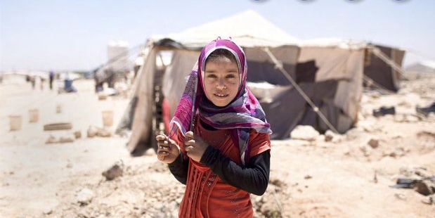 A girl in headscarf stands in front of tents in a desert landscape