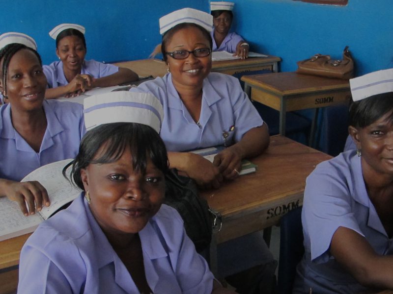 A group of seated African female nurses in uniform, smiling at the camera