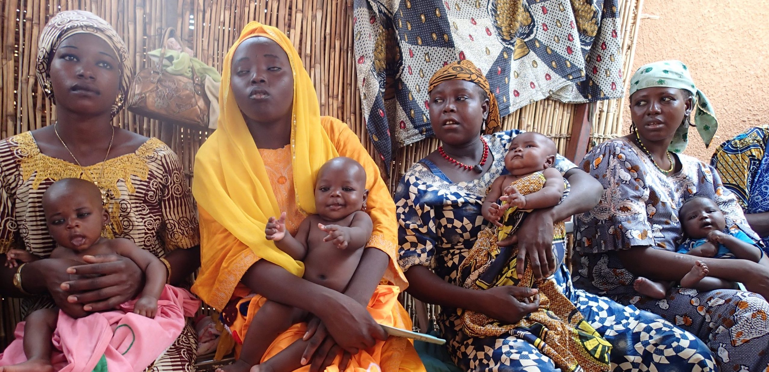 Four African women in brightly coloured clothes sitting waiting, each with a baby on their knee
