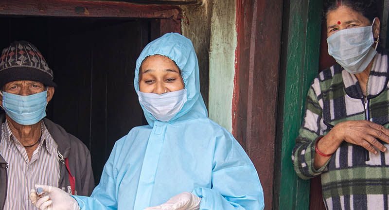 An India woman in blue PPE stands between a man and a woman both wearing face masks