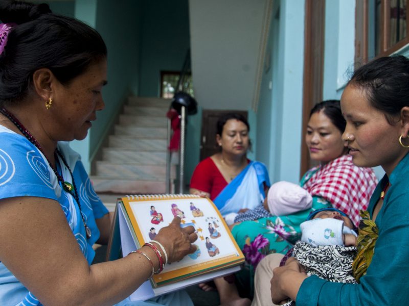 A woman in pale blue sari shows diagrams to a mother holding a baby