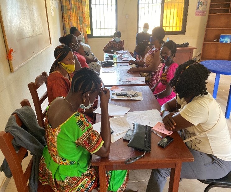 Masked African women sitting around a long table - they are talking and reading documents