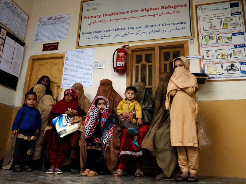 Five seated women in burkas with six children. Above them is a sign reading 'Primary healthcare for Afghan refugees'