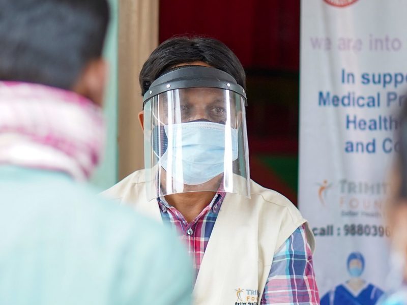 A man in full PPE talks to a woman and a man who have their backs to use