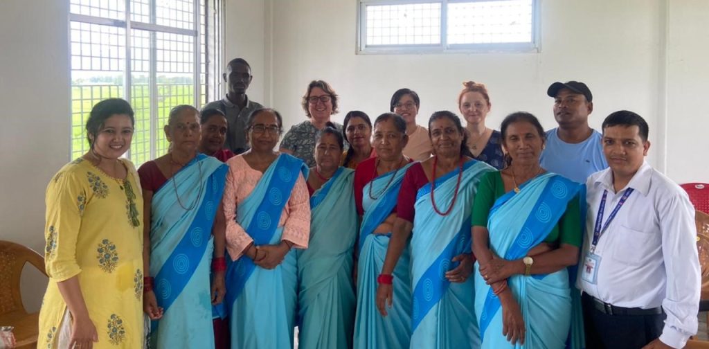 A row of standing smiling Nepali women in blue saris, surrounded by other men and women 