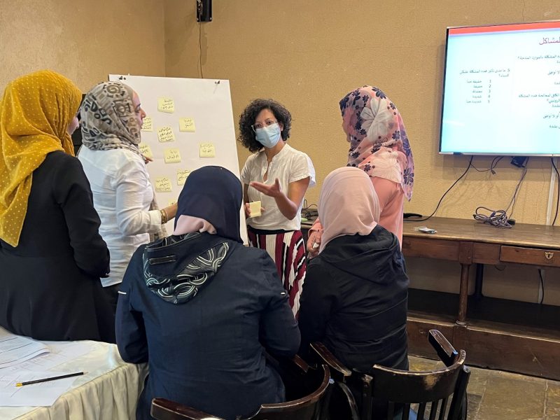 Standing women wearing hijabs stand with their backs to the camera while they look at flipchart