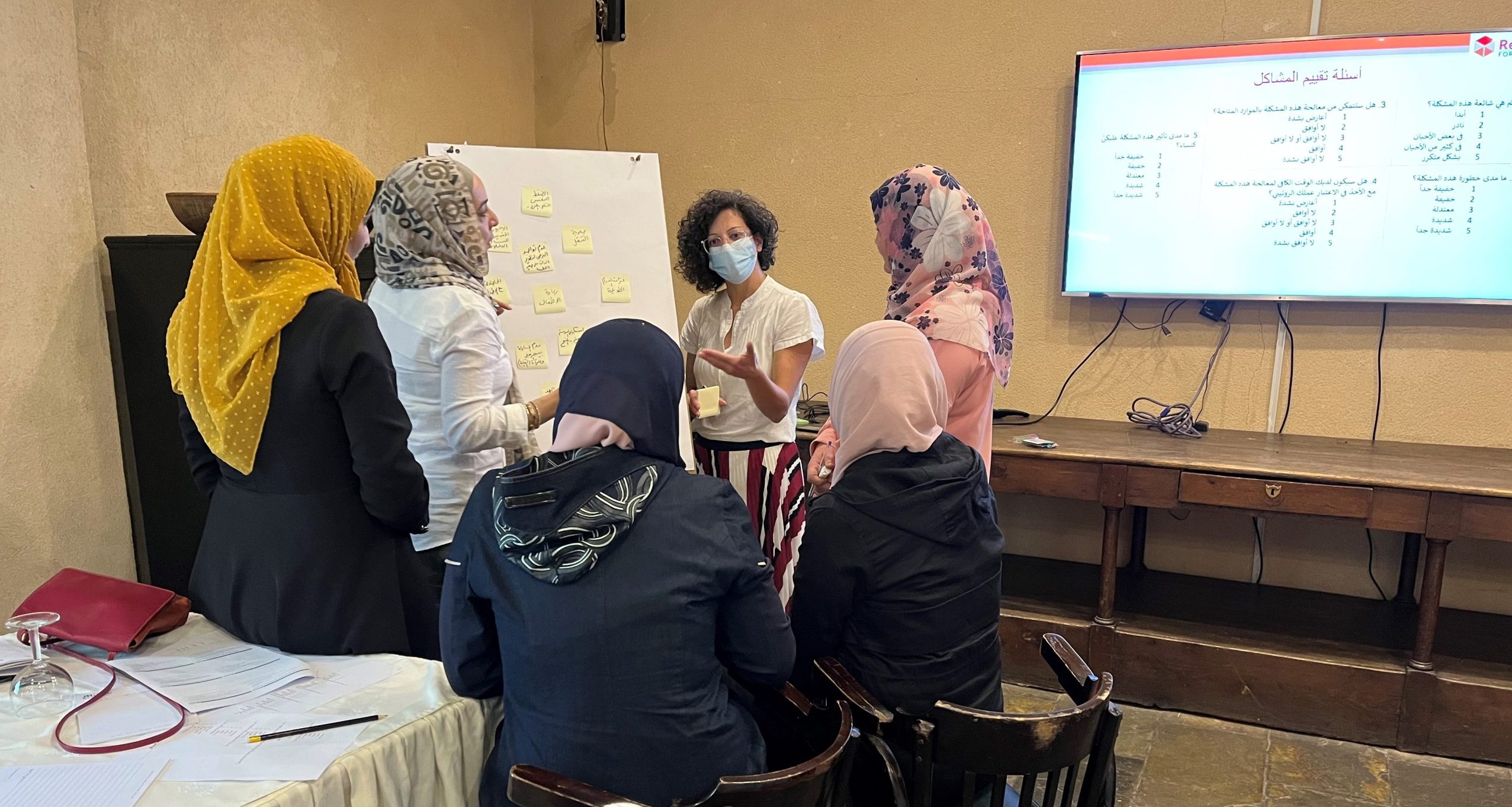 Standing women wearing hijabs stand with their backs to the camera while they look at flipchart