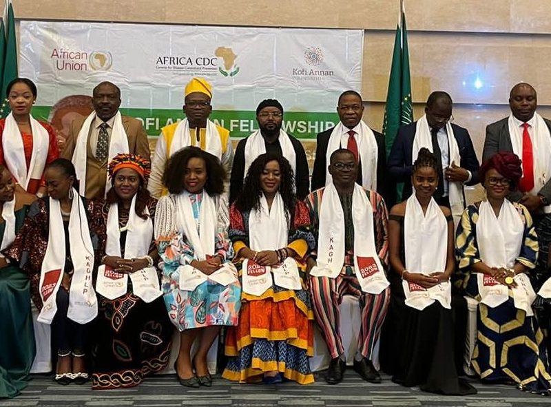 A group 18 African men and women in formal dress pose smiling for the camera