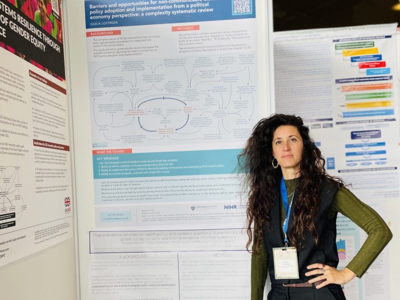 A European woman with long dark hair standing next to a poster