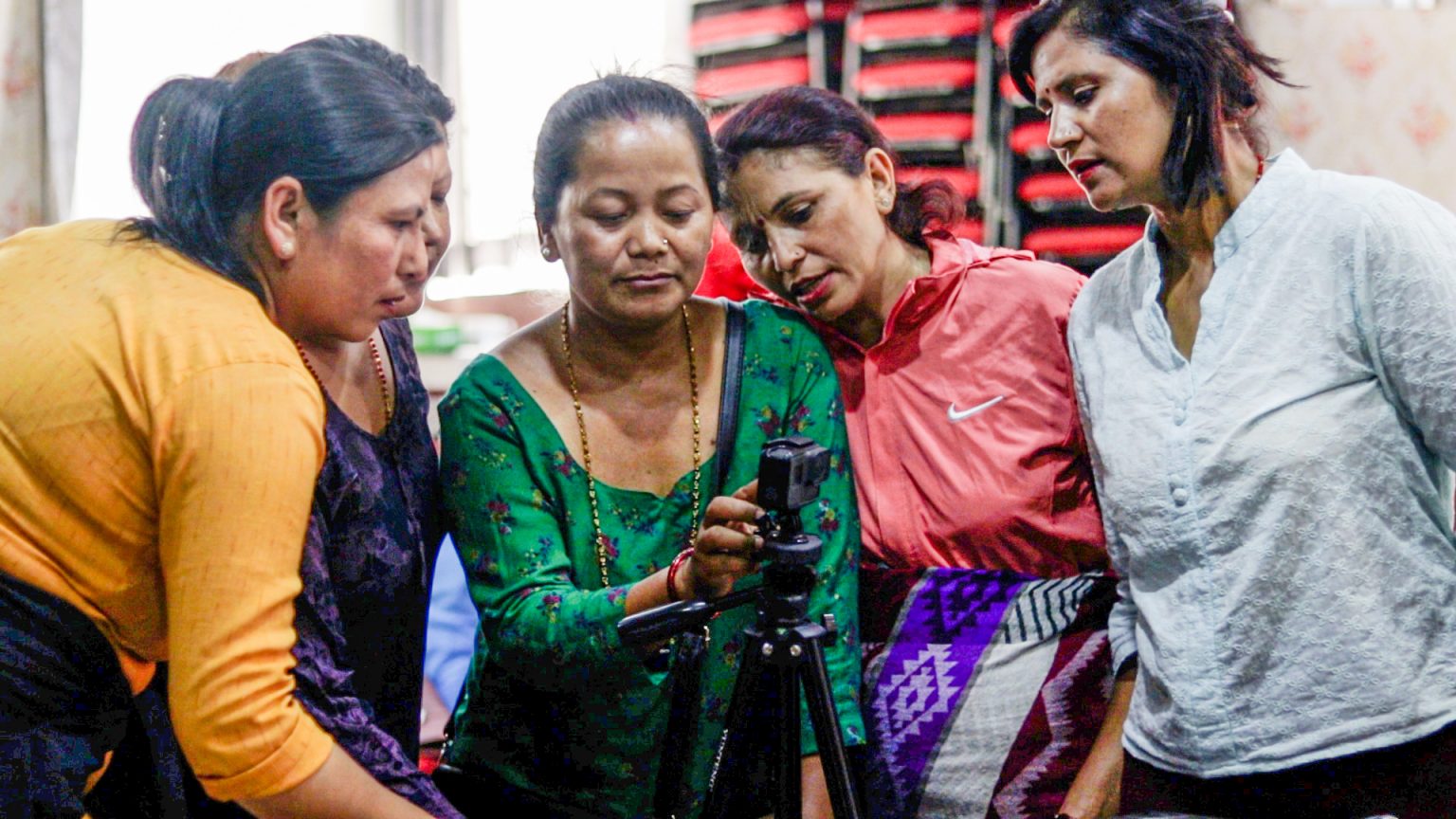 Five Nepali women in saris examining a camera on a tripod
