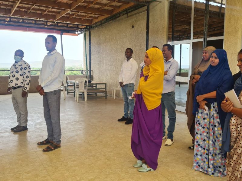 A group of 8 smiling Ethiopian men and women stand apart from each other in a large room