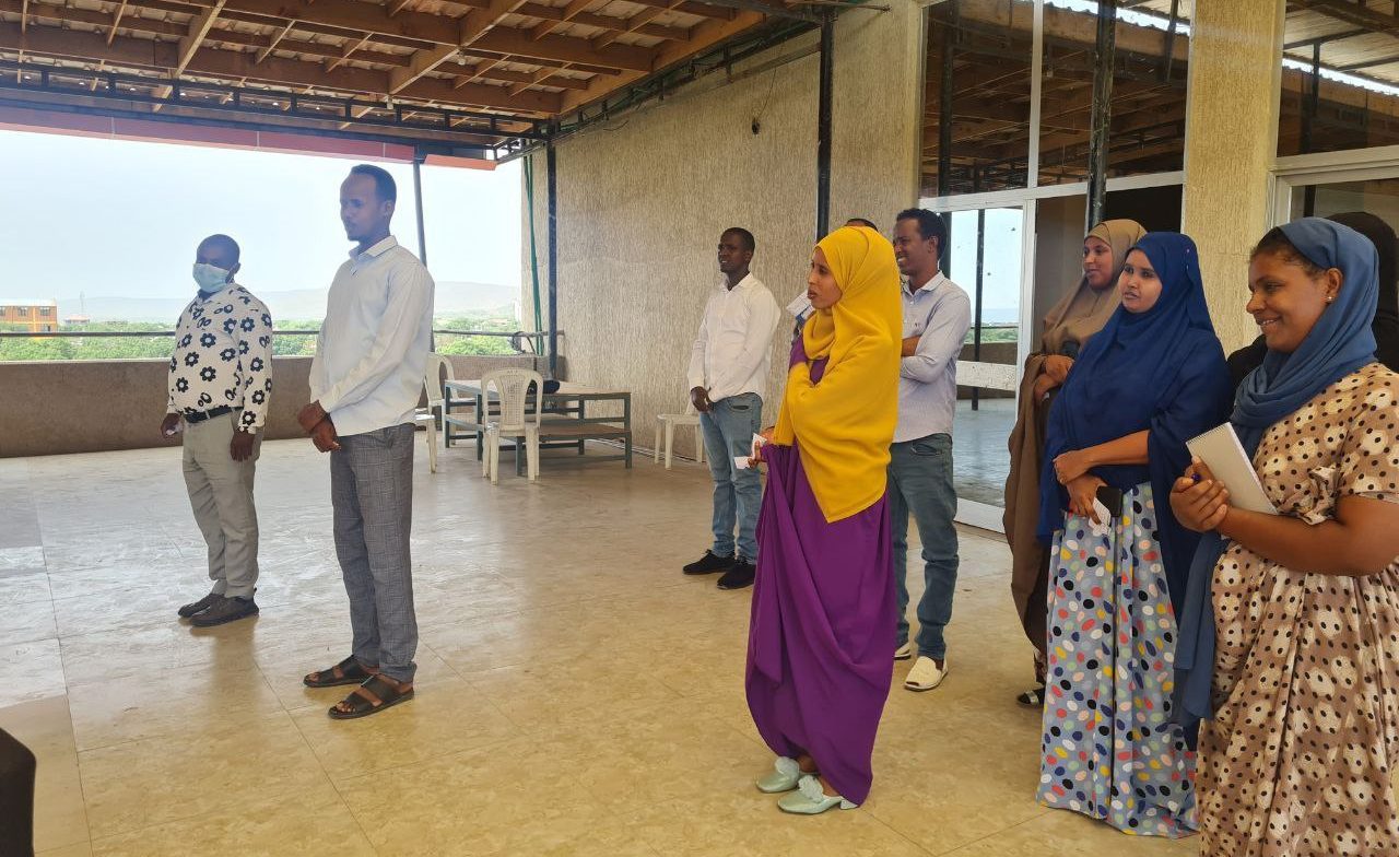 A group of 8 smiling Ethiopian men and women stand apart from each other in a large room