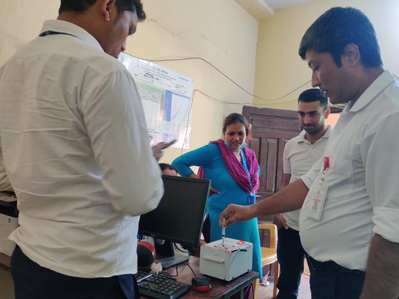 Health workers stand around a man putting a syringe into a machine