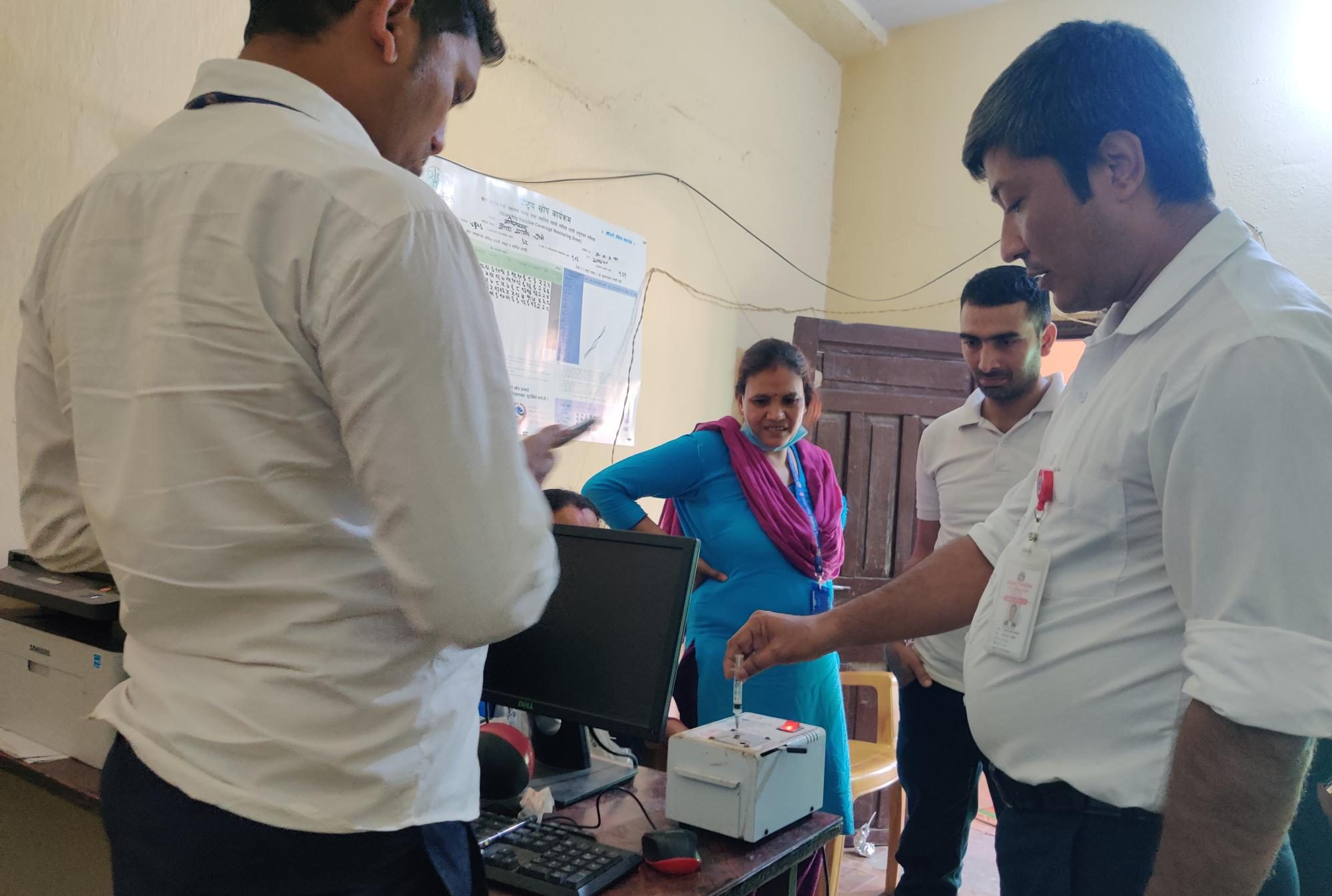 Health workers stand around a man putting a syringe into a machine