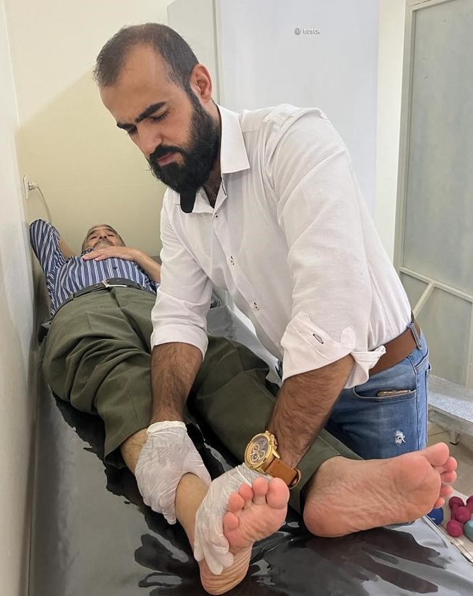 A man examining the ankle of another man who is laying down 