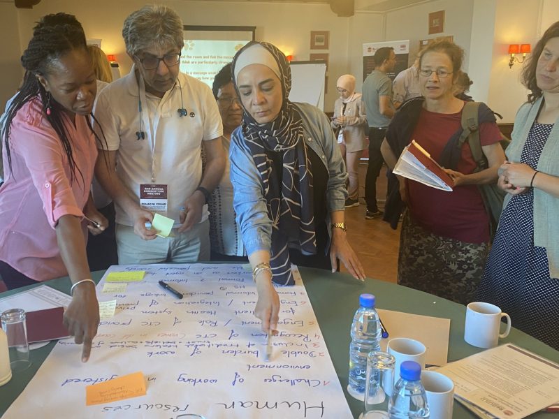 Four women and a man stand around a sheet of flipchart paper - 2 of the women are pointing to it