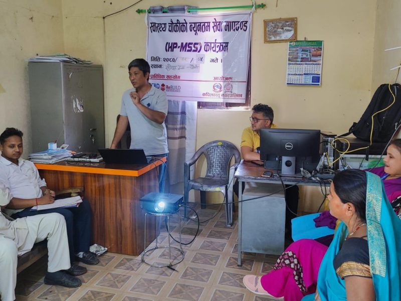 Nepali women and men sit in an office. One man stands talking