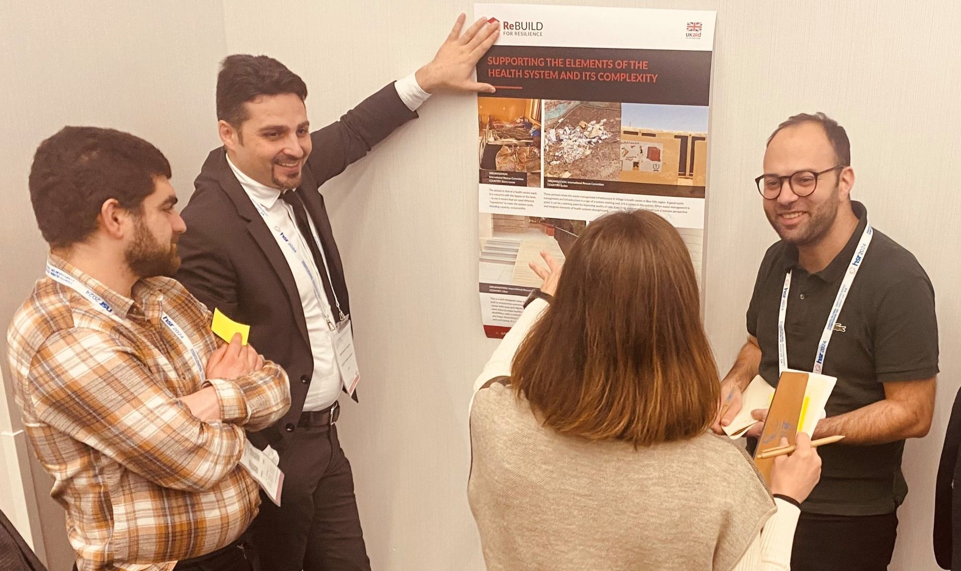 Smiling men and women standing around a poster being held on the wall