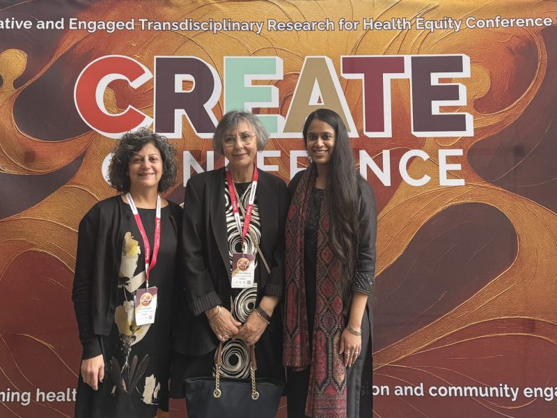 Three women stand smiling in front of a large banner with the words 'Create conference' on it