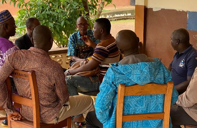A group of men in Sierra Leone sit talking in a group outside a building