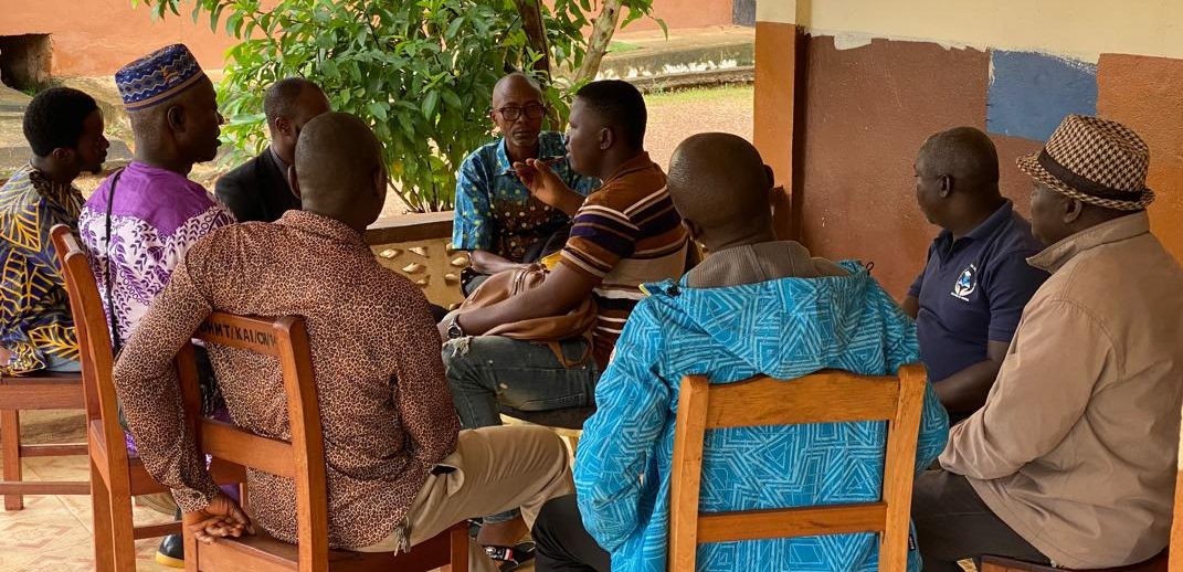 A group of men in Sierra Leone sit talking in a group outside a building