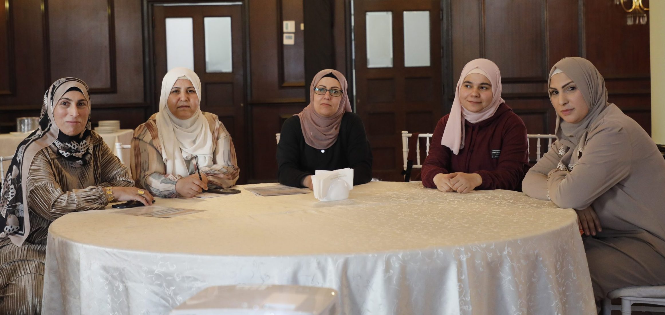 Photo of five Syrian women sitting around a table in a wood-panelled room. All are looking defiantly at the camera