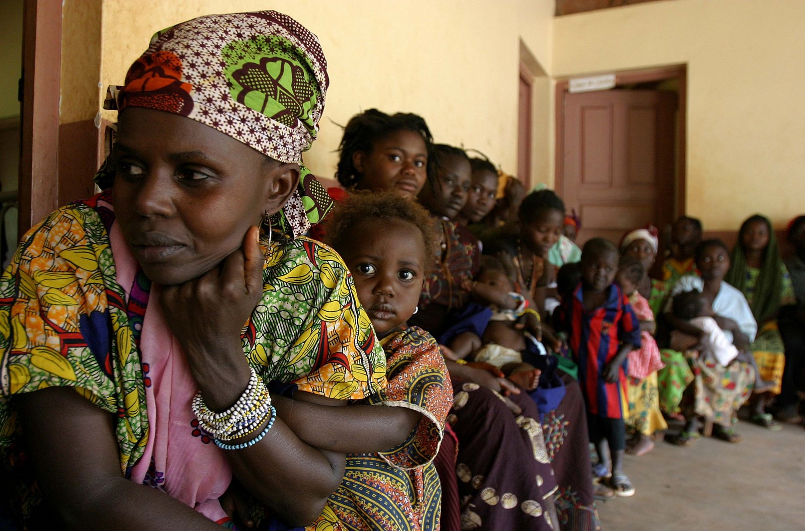 A doctor's waiting room in CAR. There's a long queue of seated women and small children - some are looking at the camera. It is part of a Mother and Child Survival Campaign, managed by UNICEF CAR in collaboration with the Ministry of Health, UNFPA and WHO.