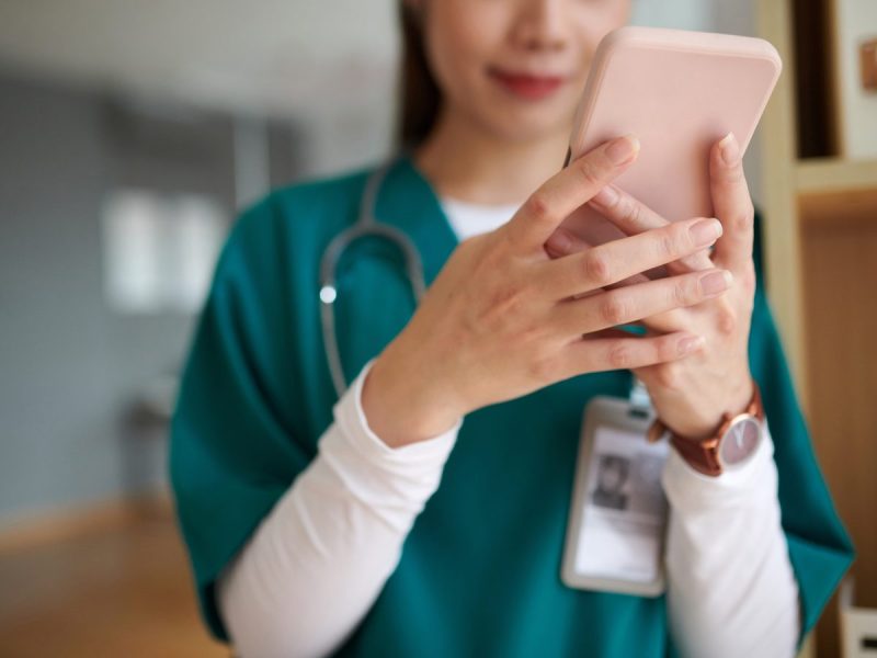 Photograph of a female medic in green uniform looking at their pink phone
