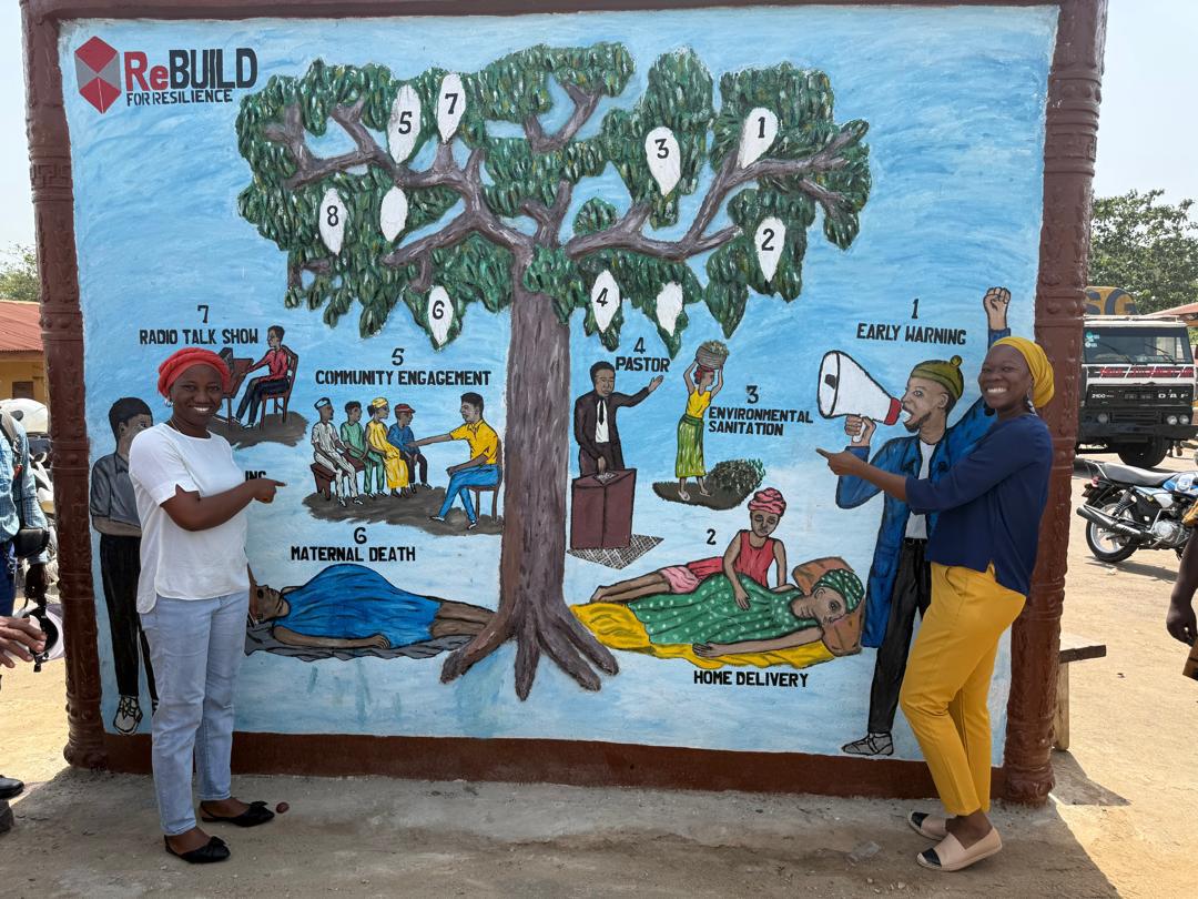 Two Sierra Leonian women standing in front of a mural of a tree
