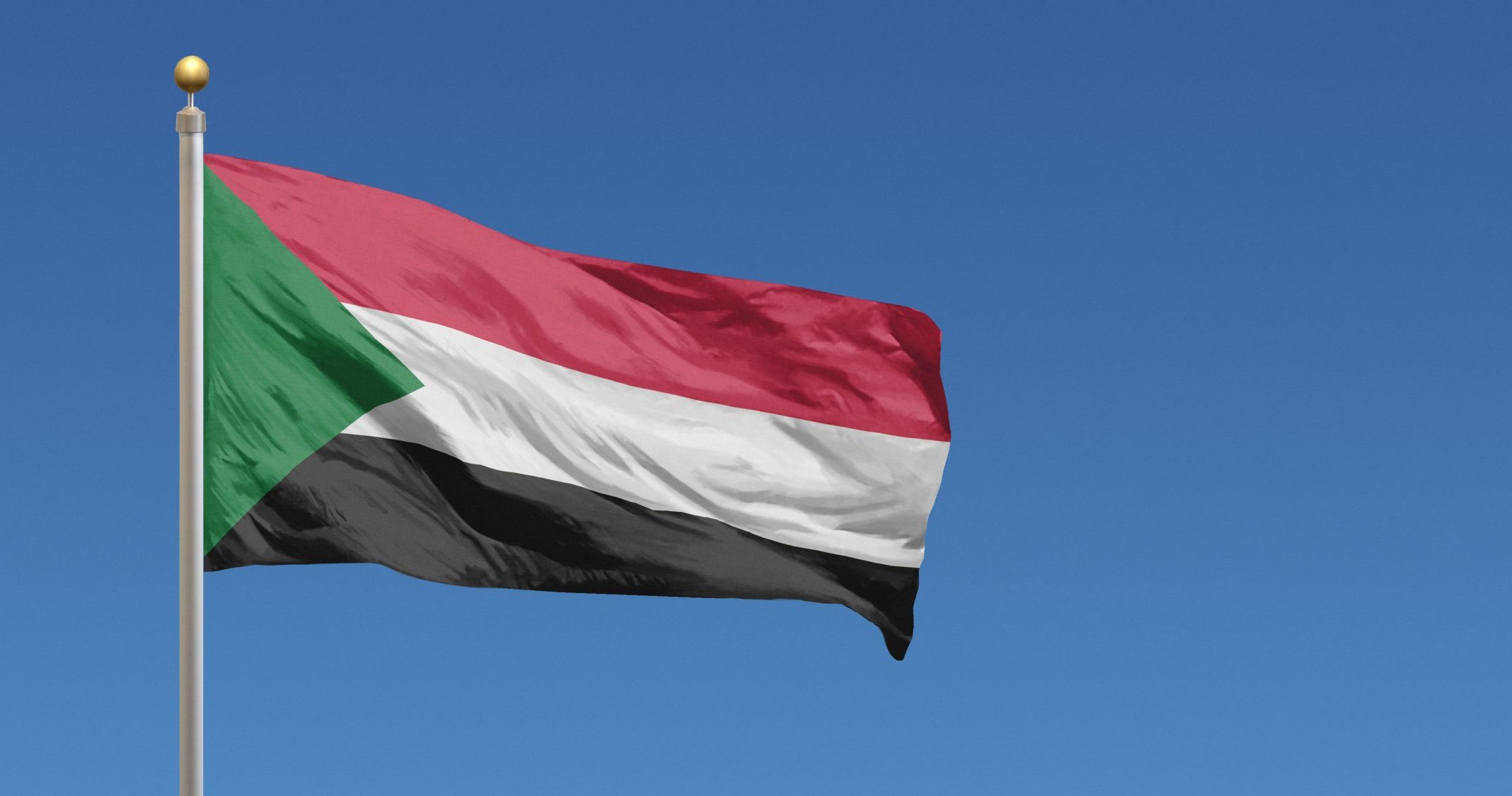 The green, red, white and black flag of Sudan against a blue sky
