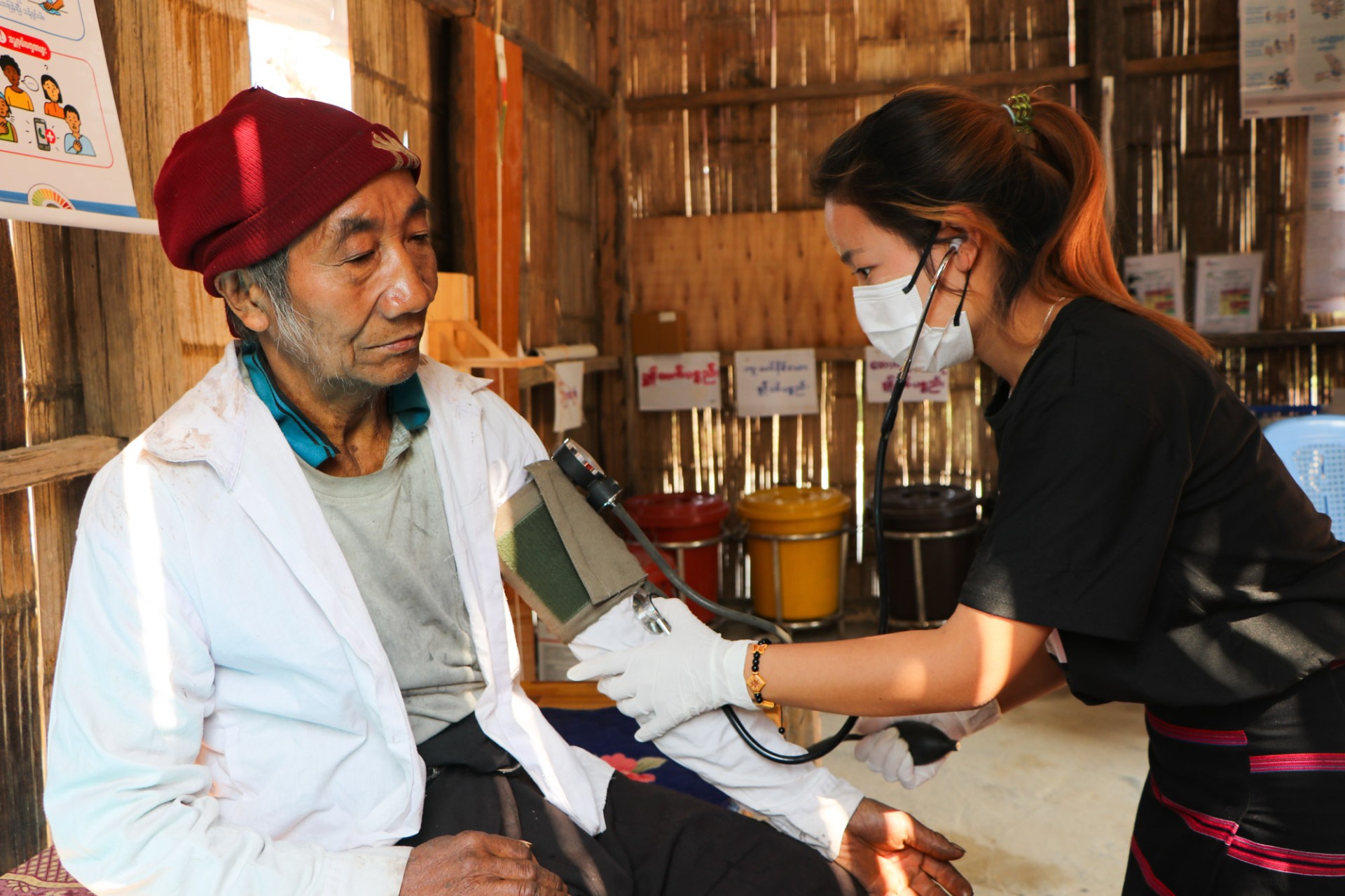 A female doctor wearing a face mask takes the blood pressure of an old man on the Thailand-Myanmar border