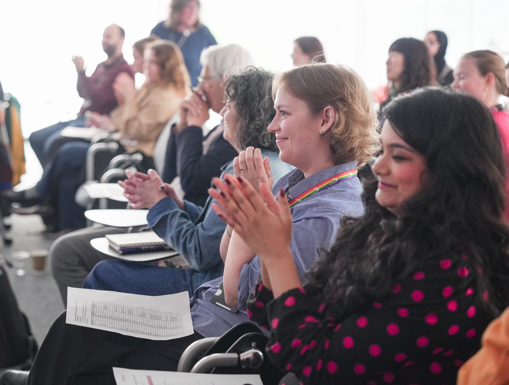 A row of seated, smiling , clapping researchers - all are looking towards something off camera